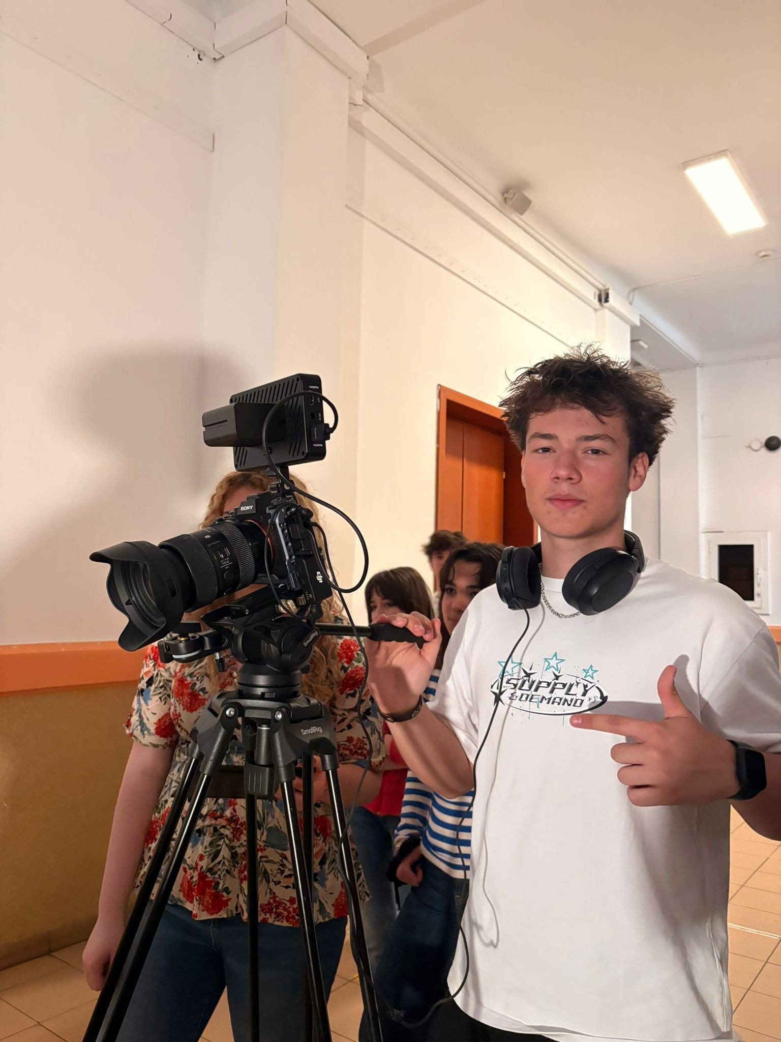 Alexandru Moise lângă camera de filmat, pe hol, alături de echipa de filmare, în timpul unui proiect.